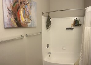 A bathroom with a white bathtub, a shower curtain, a towel rack, a shower head, and a shelf with toiletries. - Super Bowl weekend! (Phoenix)