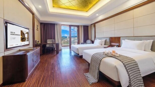 Habitación de hotel con dos camas, televisión, escritorio y vistas a la ciudad.