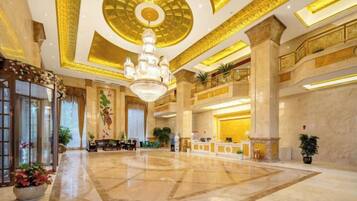 A spacious lobby with a grand chandelier, marble flooring, and a reception desk.
