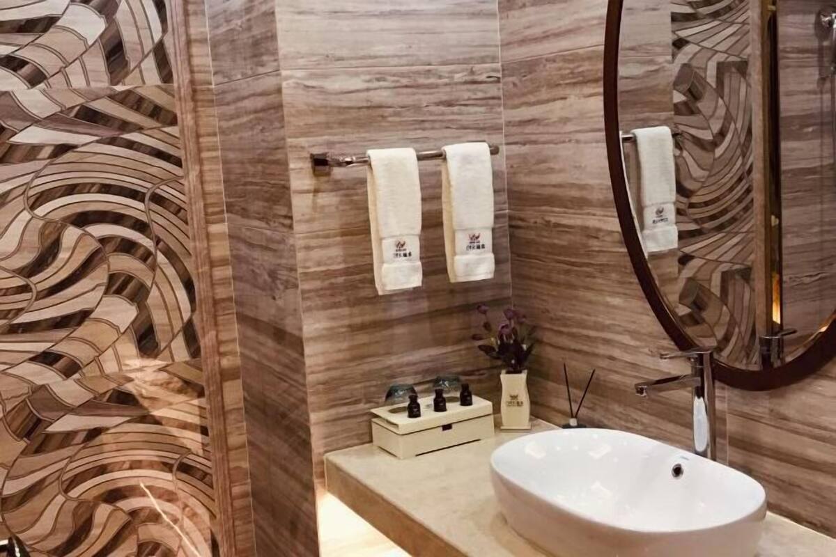 Ein Badezimmer mit Marmorwand, einem Waschbecken, einem Spiegel und zwei Handtüchern, die auf einem Handtuchhalter hängen.