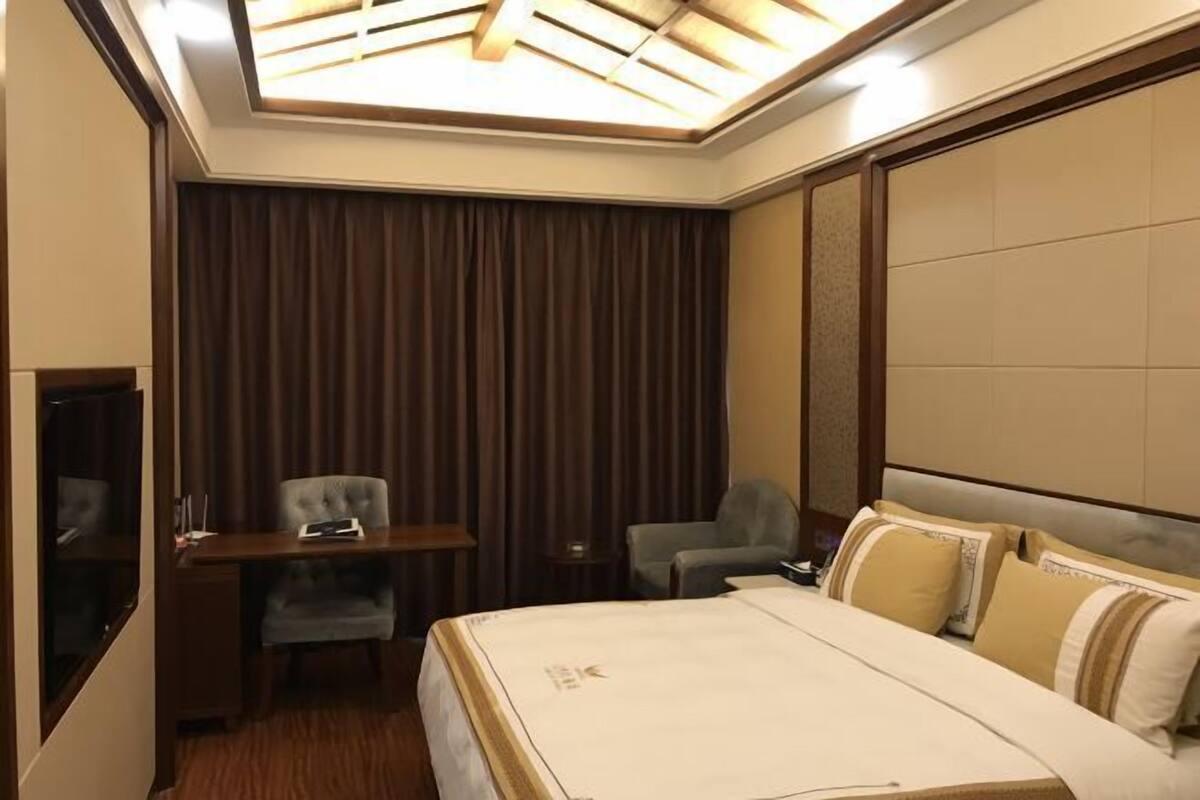 Ein Hotelzimmer mit einem großen Bett, einem Schreibtisch mit Stuhl, einem Fernseher und einer Deckenleuchte.