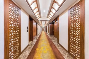 Un pasillo de hotel con paneles de madera, suelo de mármol y una larga galería que conduce a varias puertas.