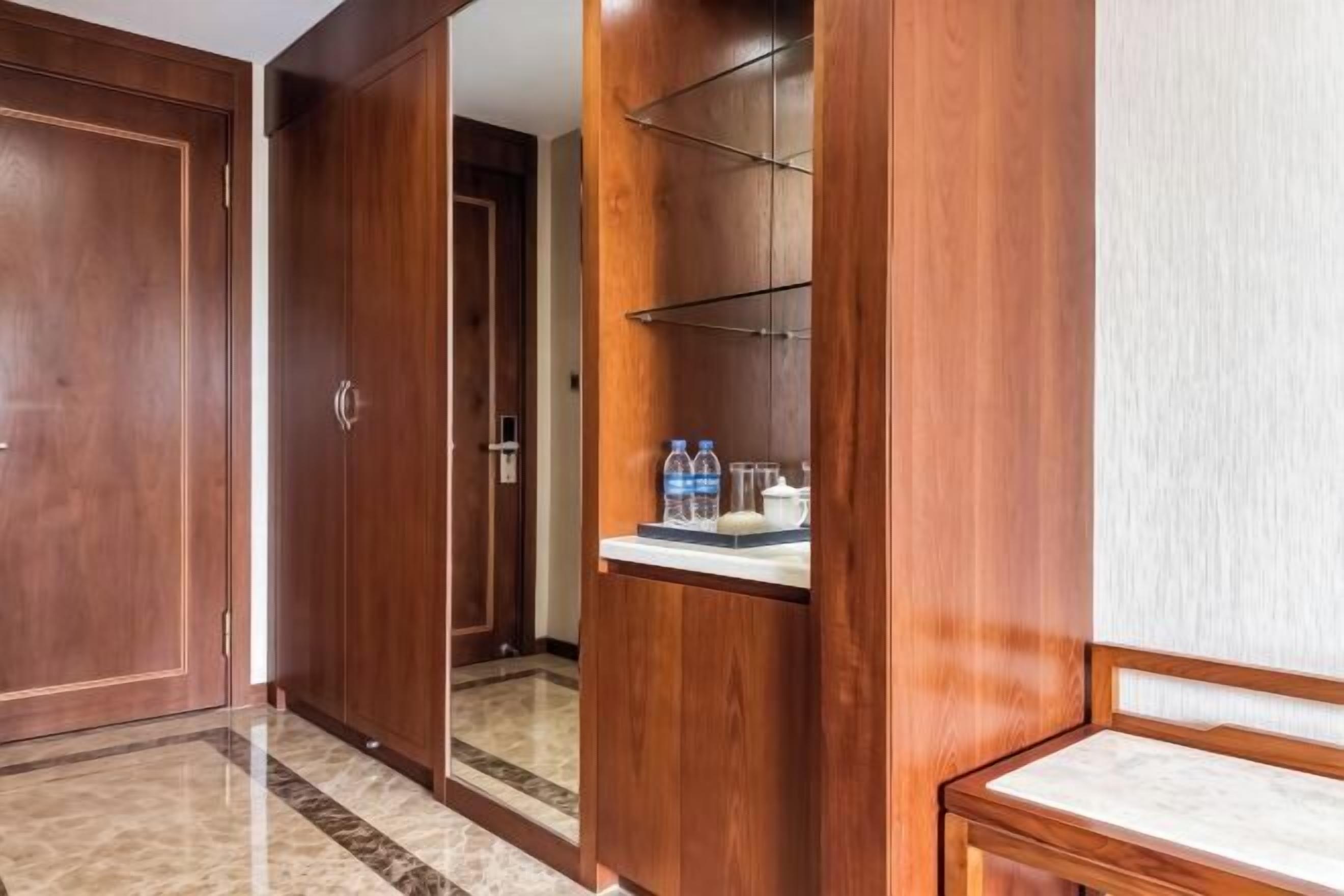 A hotel corridor with wooden doors, a mirrored wardrobe, and a small table with water bottles.