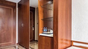 A hotel corridor with wooden doors, a mirrored wardrobe, and a small table with water bottles. - Menluo Wa Jing Luxury Grand Hotel(Hulu Town Wa Tribe Branch) (Cangyuan)