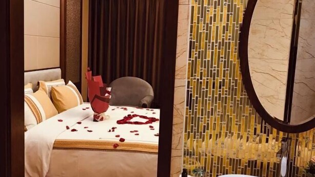 A hotel room with a bed, a chair, a bathroom with a sink, and a decorative wall. - Menluo Wa Jing Luxury Grand Hotel(Hulu Town Wa Tribe Branch) (Cangyuan)