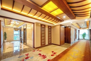 A hotel lobby with a long corridor, wooden paneling, and a patterned carpet.