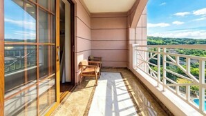 A balcony with a view of greenery and a pool, a sliding glass door, and a small table with chairs. - Menluo Wa Jing Luxury Grand Hotel(Hulu Town Wa Tribe Branch) (Cangyuan)
