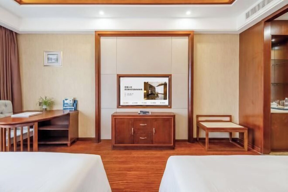 Habitación de hotel con un escritorio de madera, un televisor montado en la pared, una cama y un pequeño rincón de descanso.