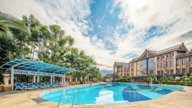 En swimmingpool med solstolar, ett avskärmat sittområde och en byggnad med flera fönster.