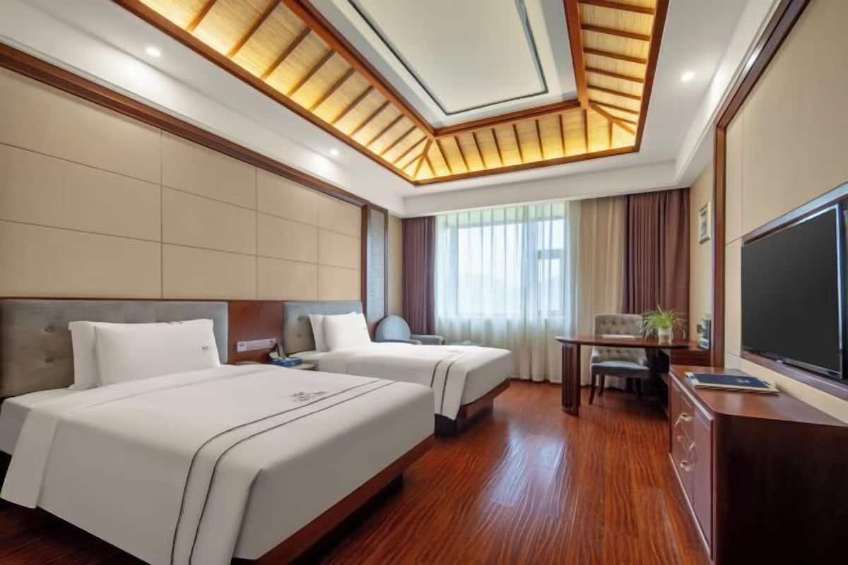 A hotel room with two beds, a desk, a TV, and a large window.