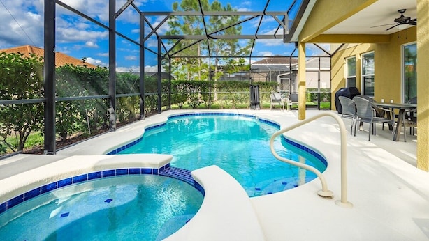 Ein Pool mit geschwungener Form, umgeben von einer überdachten Terrasse mit Gartenmöbeln.