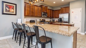 Eine moderne Küche mit Granit Arbeitsplatten, Holzschränken, einem Edelstahlkühlschrank und einer Bar mit Hockern.
