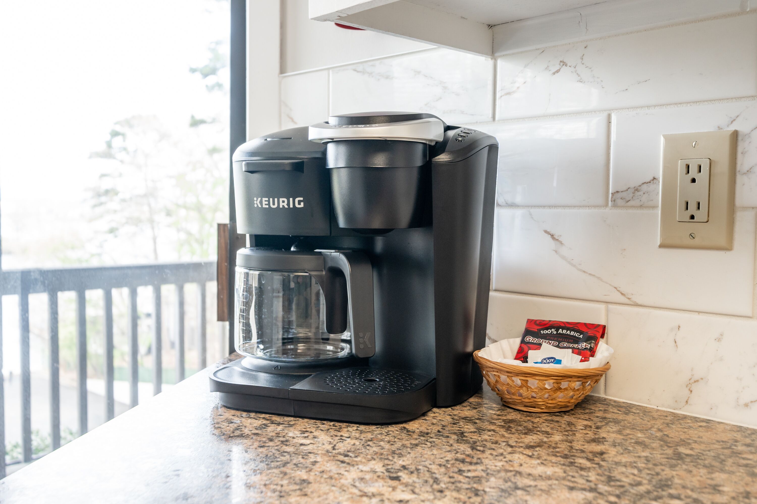 Eine Kaffeemaschine von Keurig steht auf einer Granit-Arbeitsplatte neben einem Korb mit einer Kaffeekapsel.