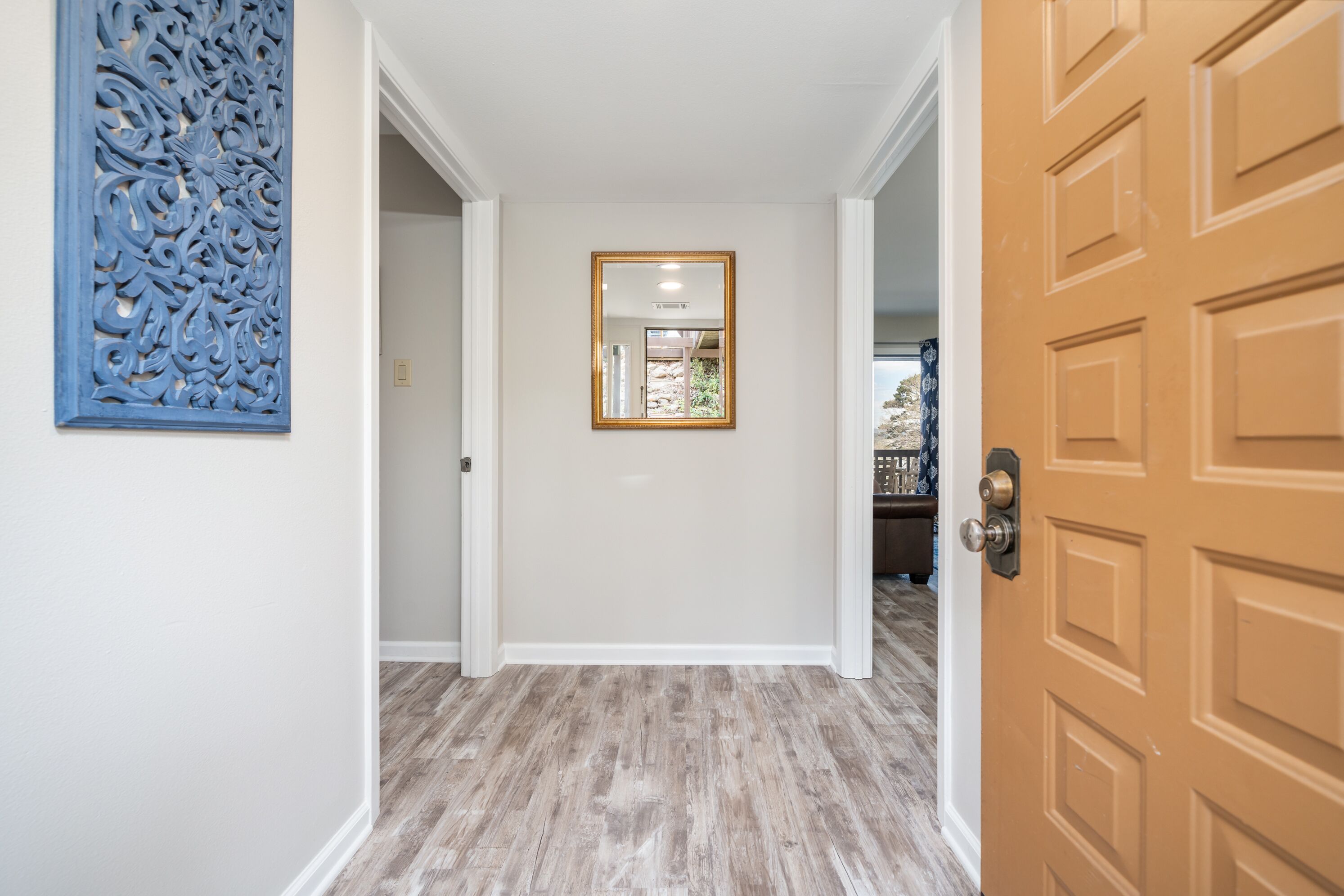 A hallway with a wooden floor, a decorative blue panel, and a framed mirror on the wall.