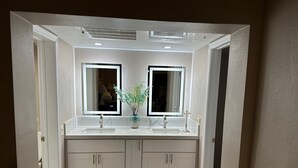 Un baño con dos lavamanos, un espejo y una ventana.