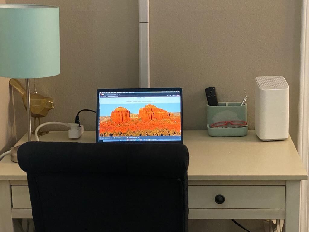 A desk with a laptop displaying a desert landscape, a lamp, a remote control holder, and a white speaker.