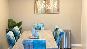 Un comedor con una mesa, sillas, un letrero en la pared y un cubo de basura.