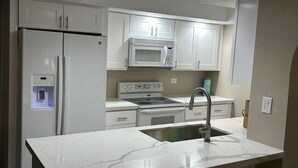 Una cocina moderna con muebles blancos, microondas integrado, estufa de acero inoxidable, refrigerador y dispensador de agua.