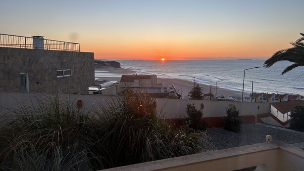 Blick auf die Küste mit Sonnenuntergang, Gebäuden und einem Strand.