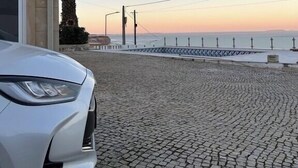 Ein weißes Auto parkt auf einer Kopfsteinpflasterstraße mit Blick auf das Meer und eine Promenade im Hintergrund.