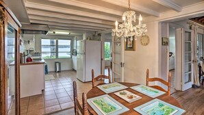 A dining area with a wooden table set for four, surrounded by wooden chairs. A chandelier hangs from the ceiling, and a kitchen is visible in the background. - Waterfront Vacation Rental on Lake Mirror! (Winter Haven)