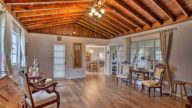 A spacious room with wooden flooring, a high ceiling with exposed beams, and a chandelier. There are several wooden chairs and a dining table with chairs. - Waterfront Vacation Rental on Lake Mirror! (Winter Haven)