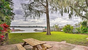 A picnic table in a grassy yard with a lake view, a dock, and a wooden fence. - Waterfront Vacation Rental on Lake Mirror! (Winter Haven)