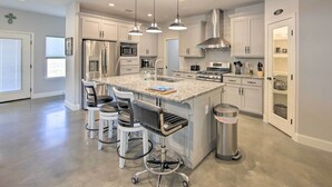 A modern kitchen with white cabinets, stainless steel appliances, a granite countertop, and pendant lighting.