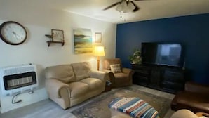A living room with a beige sofa, a patterned rug, a ceiling fan, a wall clock, a television, and a fireplace. - The Little Fish in Eufaula (Eufaula)