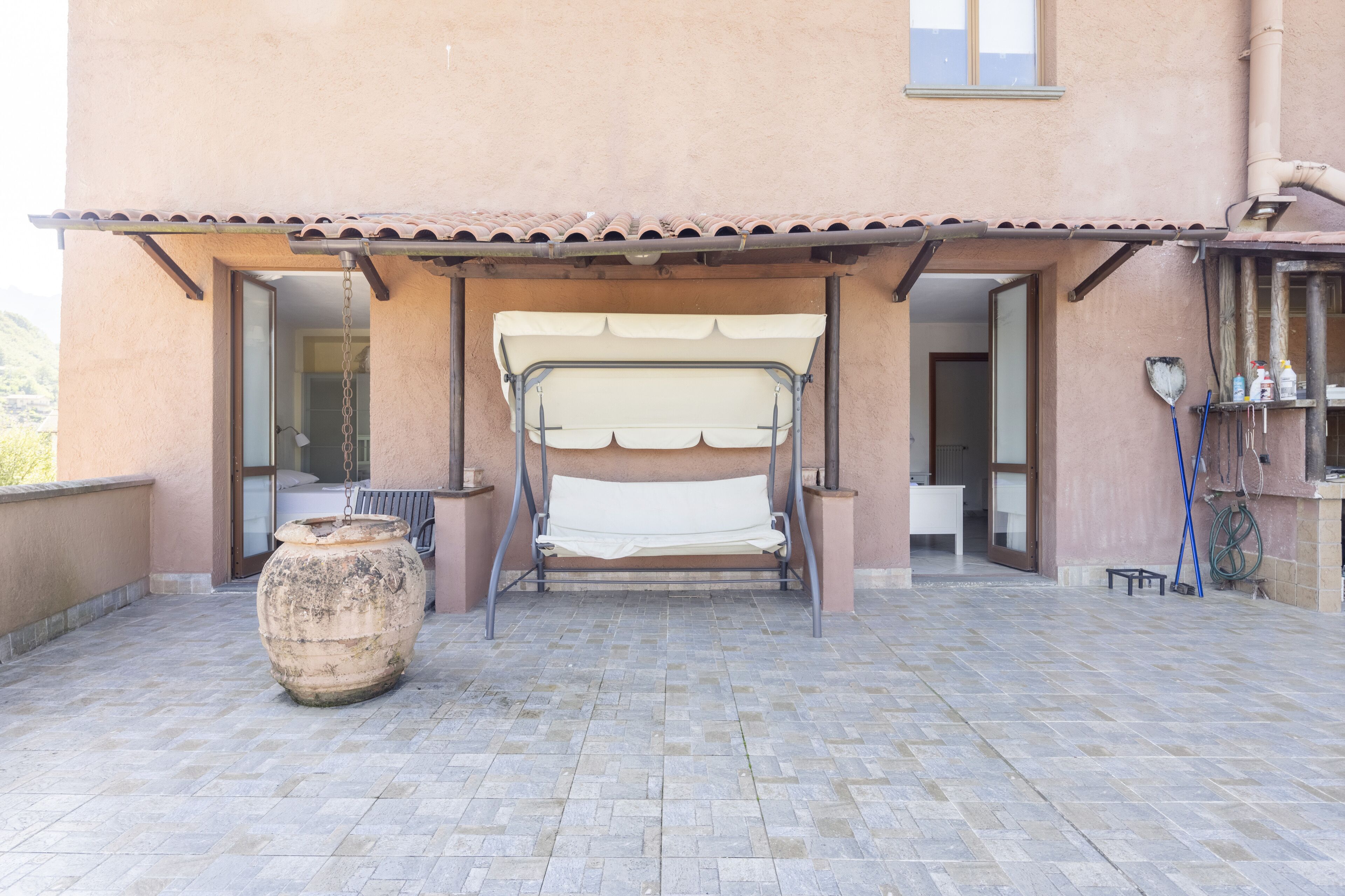 A patio with a metal bench, a large pot, and a tiled floor.