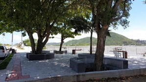 Un parque frente al agua, con árboles, macetas de concreto y vistas al mar.