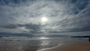 Ein Strand mit bewölktem Himmel und der Sonne am Horizont.