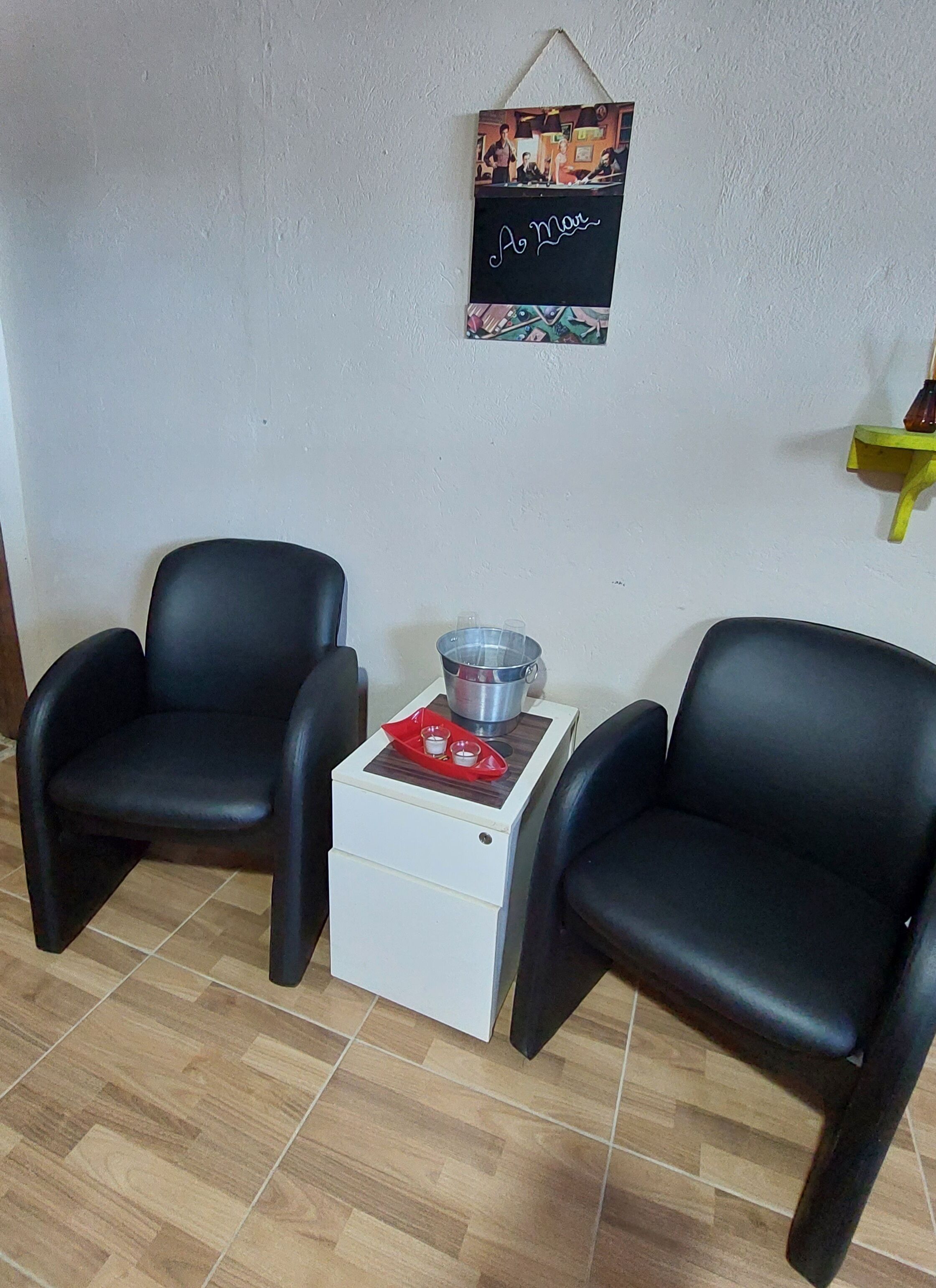 A room with two black chairs, a small white table with a red tray, and a wall-mounted picture.
