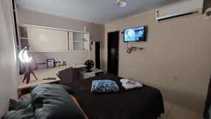 Habitación de hotel con cama, escritorio con lámpara, televisor y un pequeño ventilador.