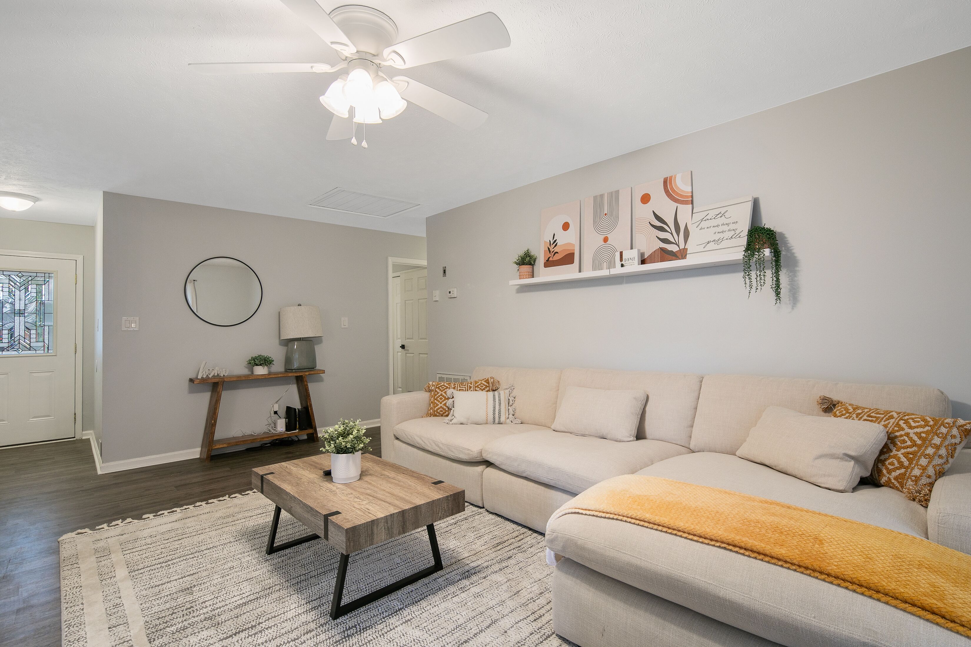 A living room with a ceiling fan, a sofa, a coffee table, and a wall-mounted shelf with decorative items.