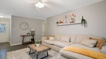 A living room with a ceiling fan, a sofa, a coffee table, and a wall-mounted shelf with decorative items.