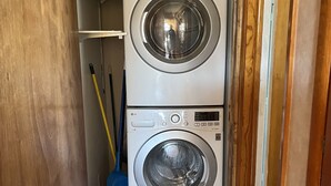 A laundry room with two stacked front-loading washing machines, a broom, and a blue dustpan. - Welcome to our Wichita Home - Easy Close Access to Turnpike South Side (Wichita)