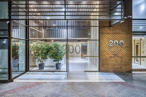 En modern entré till en byggnad med glasdörrar, en krukväxt och en tegelvägg med siffran 200.