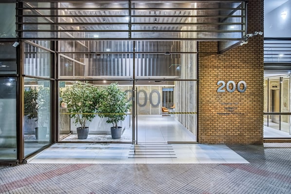 A modern building entrance with glass doors, a potted plant, and a brick wall with the number 200.