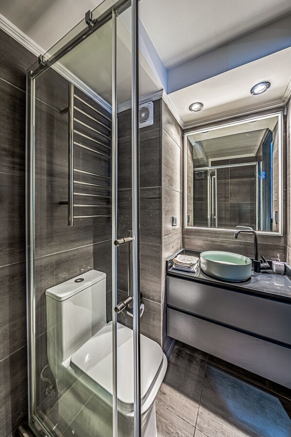 Une salle de bain moderne avec une douche à parois de verre, des toilettes blanches, un lavabo avec un miroir et un sol carrelé.