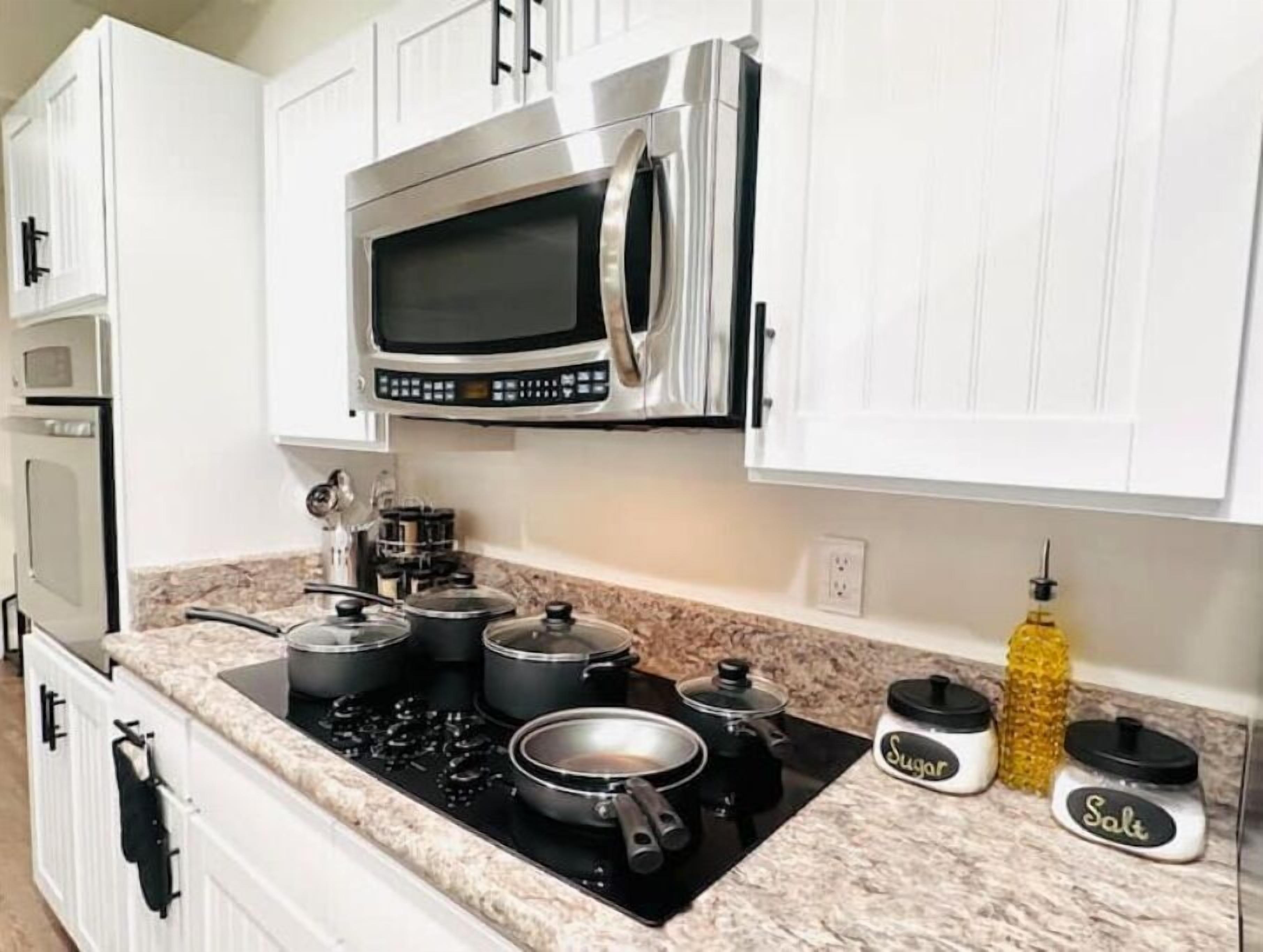 A kitchen with white cabinets, a stainless steel microwave, a stove, and pots. There are jars labeled 'Sugar' and 'Salt' on the counter.
