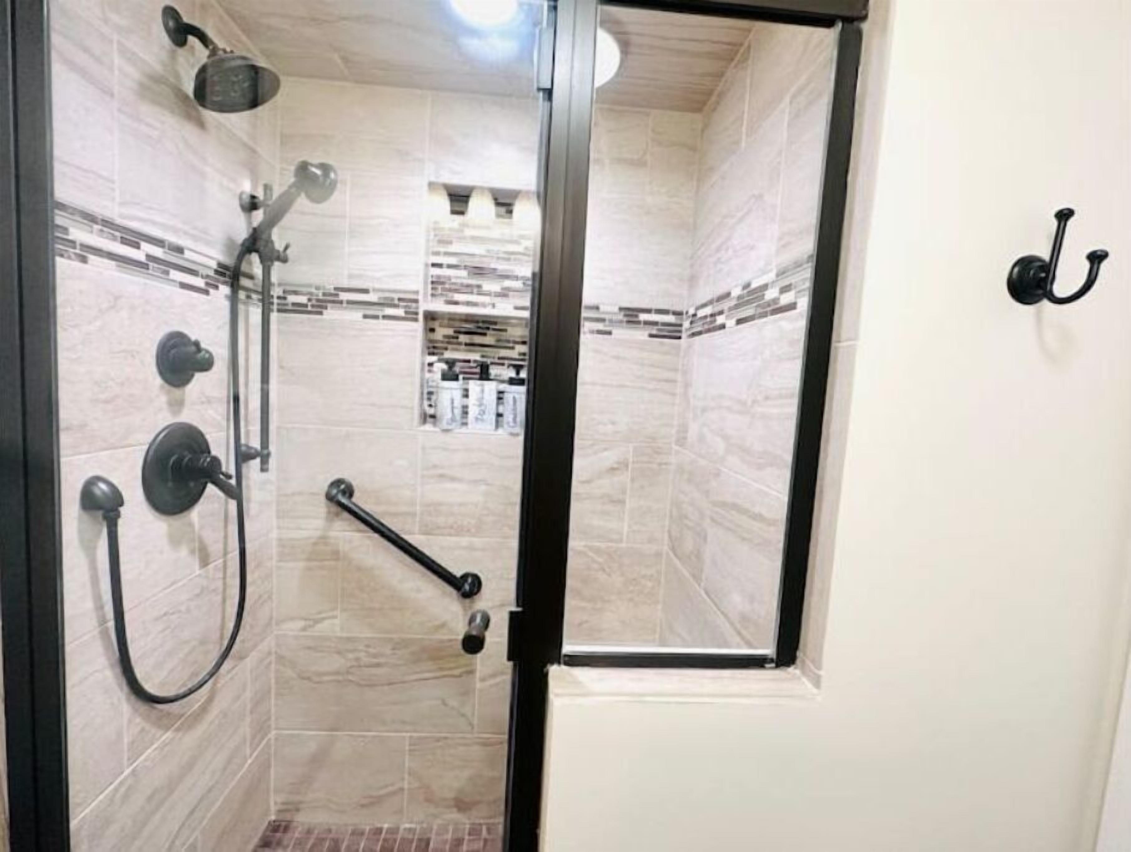 A shower area with a glass door, a handrail, and a showerhead.