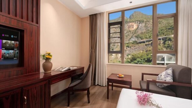 Een hotelkamer met een bureau, stoel, bed, televisie en een raam met uitzicht op de bergen.