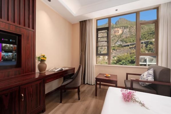 Une chambre d’hôtel équipée d’un bureau, d’une chaise, d’un lit, d’une télévision et d’une fenêtre donnant sur la montagne.