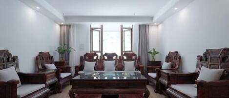 A spacious room with a large wooden table surrounded by six wooden chairs, a glass-top coffee table, and two side tables with potted plants.