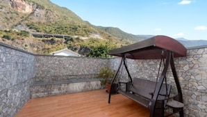 A stone-walled balcony with a wooden floor, a swing, and a potted plant. - Fall In Love With Nujiang Grand Canyon Hotel (Lushui)