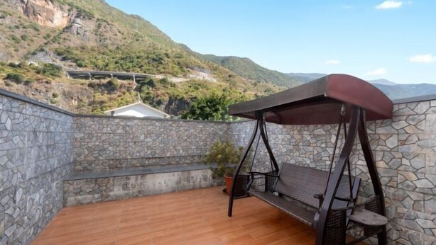 Un balcon aux murs de pierre, doté d’un plancher en bois, d’une balançoire et d’une plante en pot.