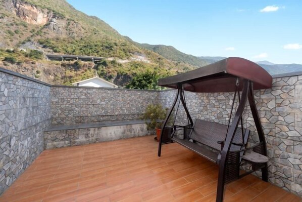 A stone-walled balcony with a wooden floor, a swing, and a potted plant. - Fall In Love With Nujiang Grand Canyon Hotel (Lushui)