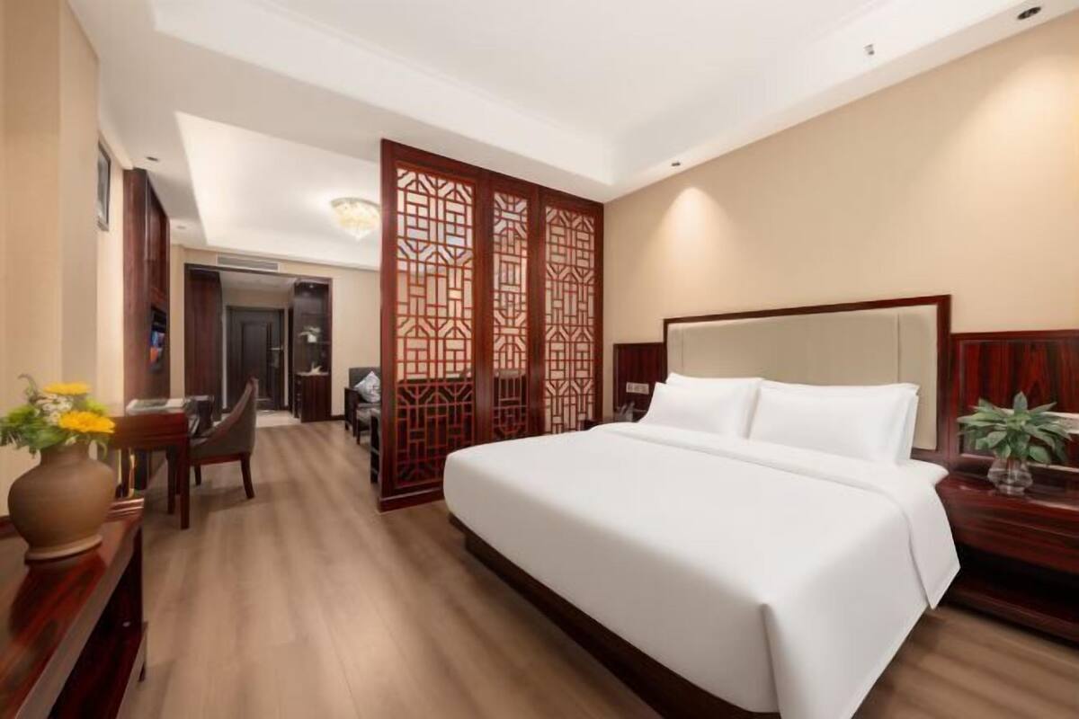 Ein Hotelzimmer mit einem großen Bett, einem Holzkopfteil, einem Schreibtisch mit Stuhl und einem dekorativen Raumteiler.