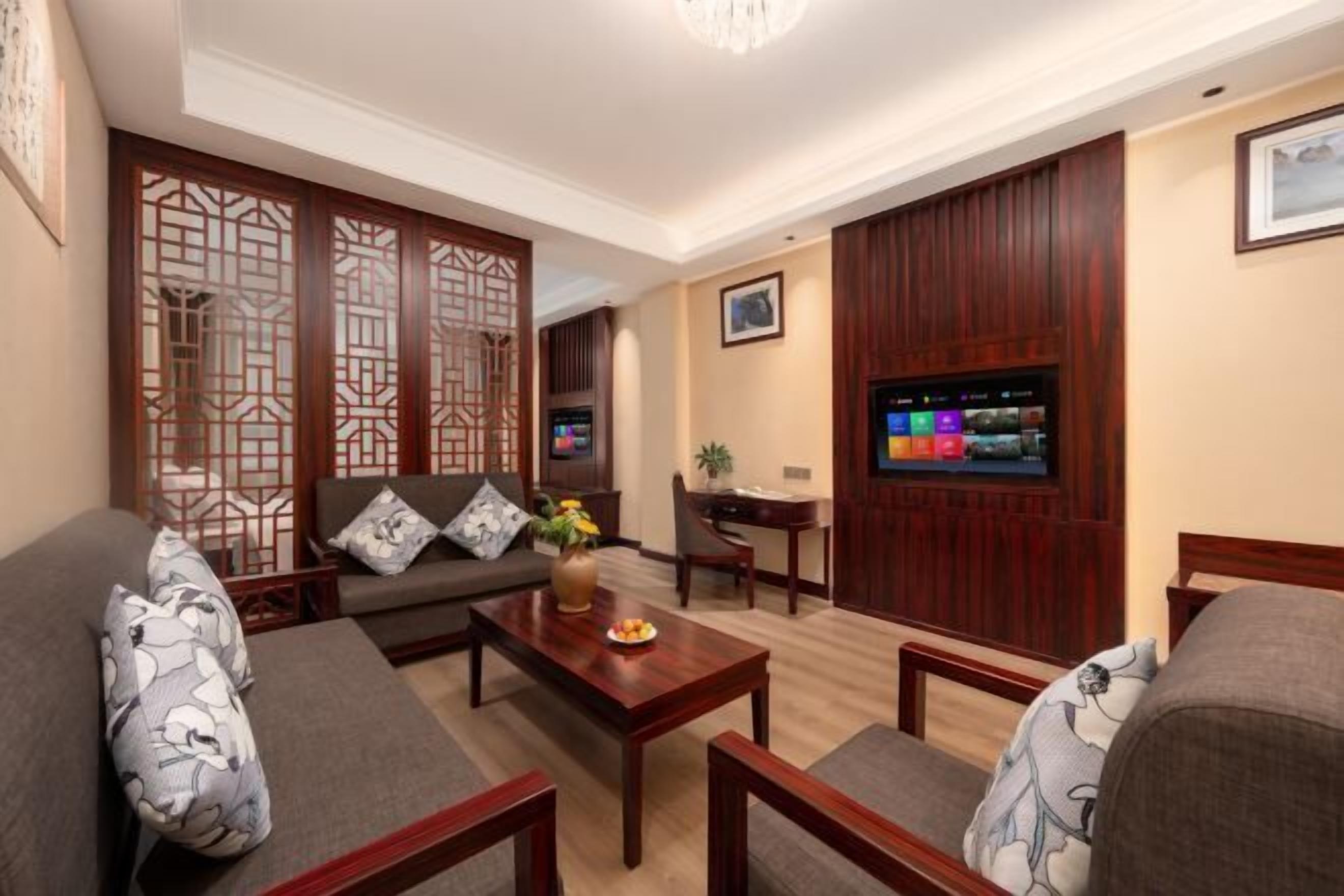 Ein Wohnzimmer mit einer Couch, Sesseln, einem Couchtisch mit einer Vase, einem Fernseher und einer Holzvertäfelung.
